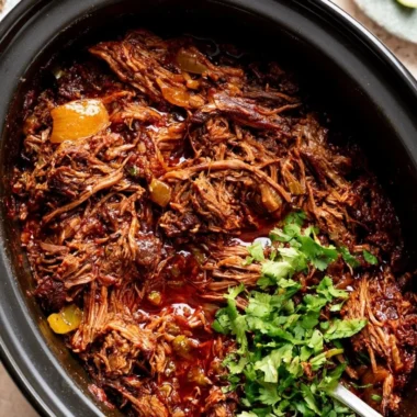A bowl of cozy beef barbacoa served with tortillas and fresh toppings.