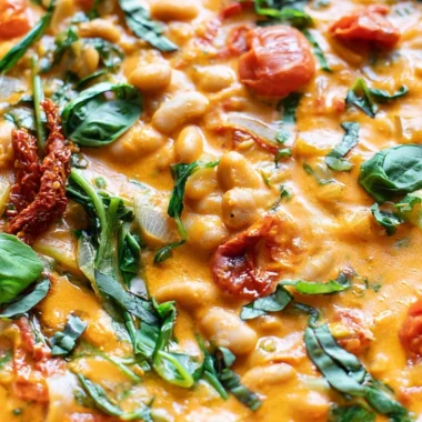 Creamy vegan tomato stew with white beans in a bowl, garnished with fresh herbs