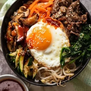 Korean Bibimbap served with colorful vegetables and a fried egg on top.
