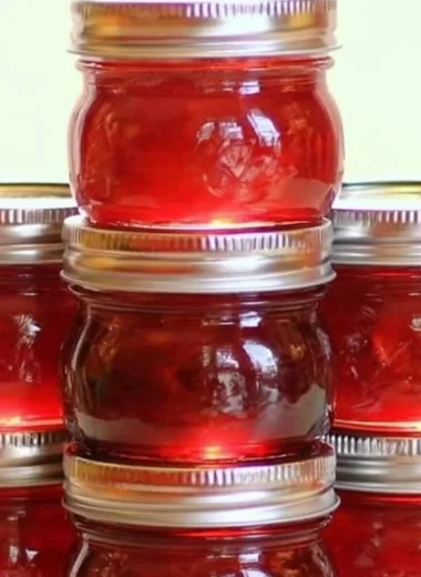 Jar of homemade rhubarb cinnamon jam on a wooden table with fresh rhubarb