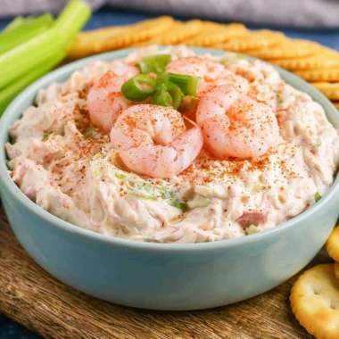 Creamy shrimp dip served in a bowl with crackers and garnished with herbs