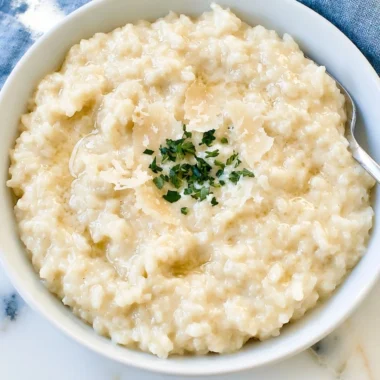 A bowl of creamy Parmesan Risotto garnished with herbs and Parmesan cheese